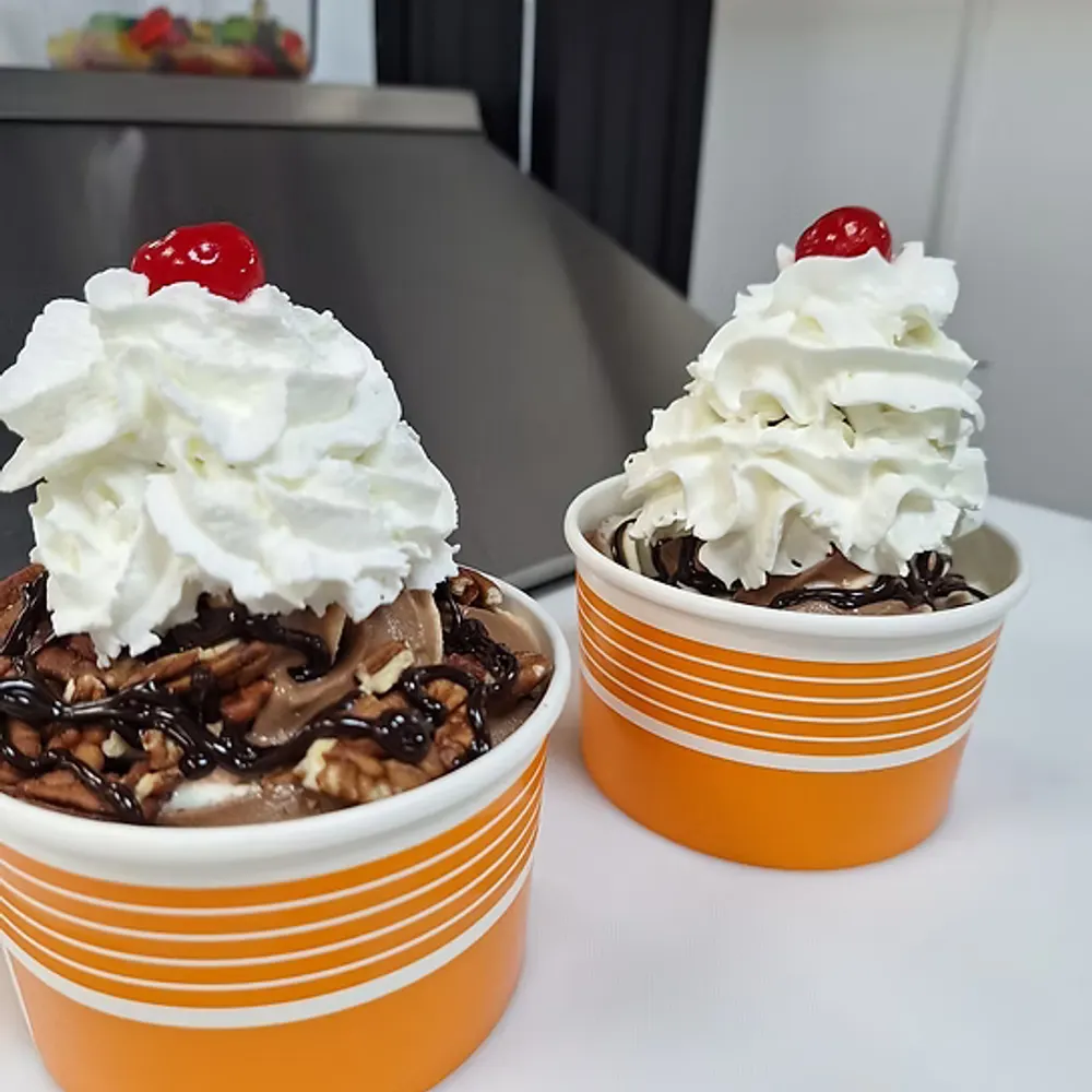 Two chocolate sundaes topped with whipped cream and cherries